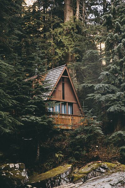 A cozy A-frame cabin nestled among tall evergreen trees in a dense forest, with a balcony featuring wooden railings.